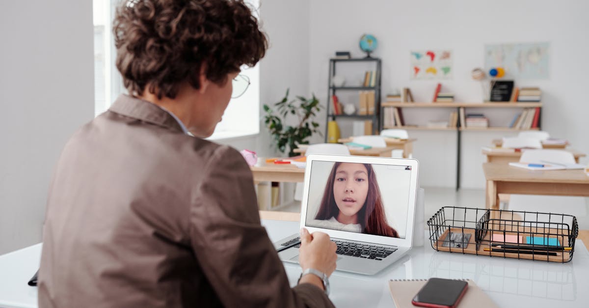 A teacher engages in an online class from an empty classroom, using a laptop for learning.